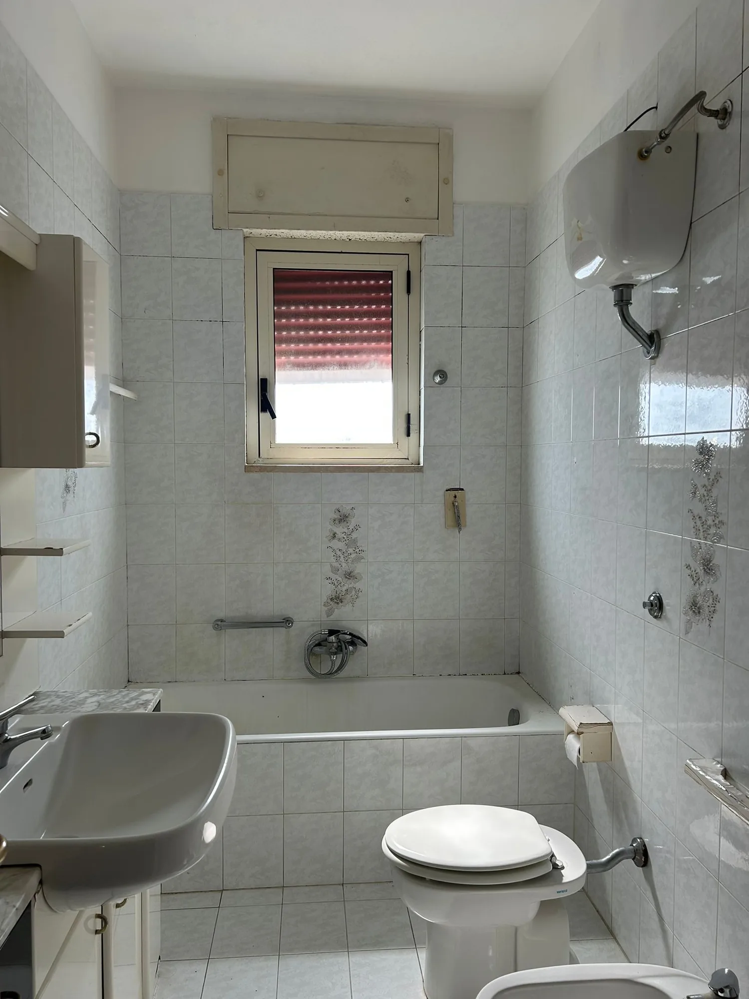 Bathroom before the intervention, with tub and light tile covering