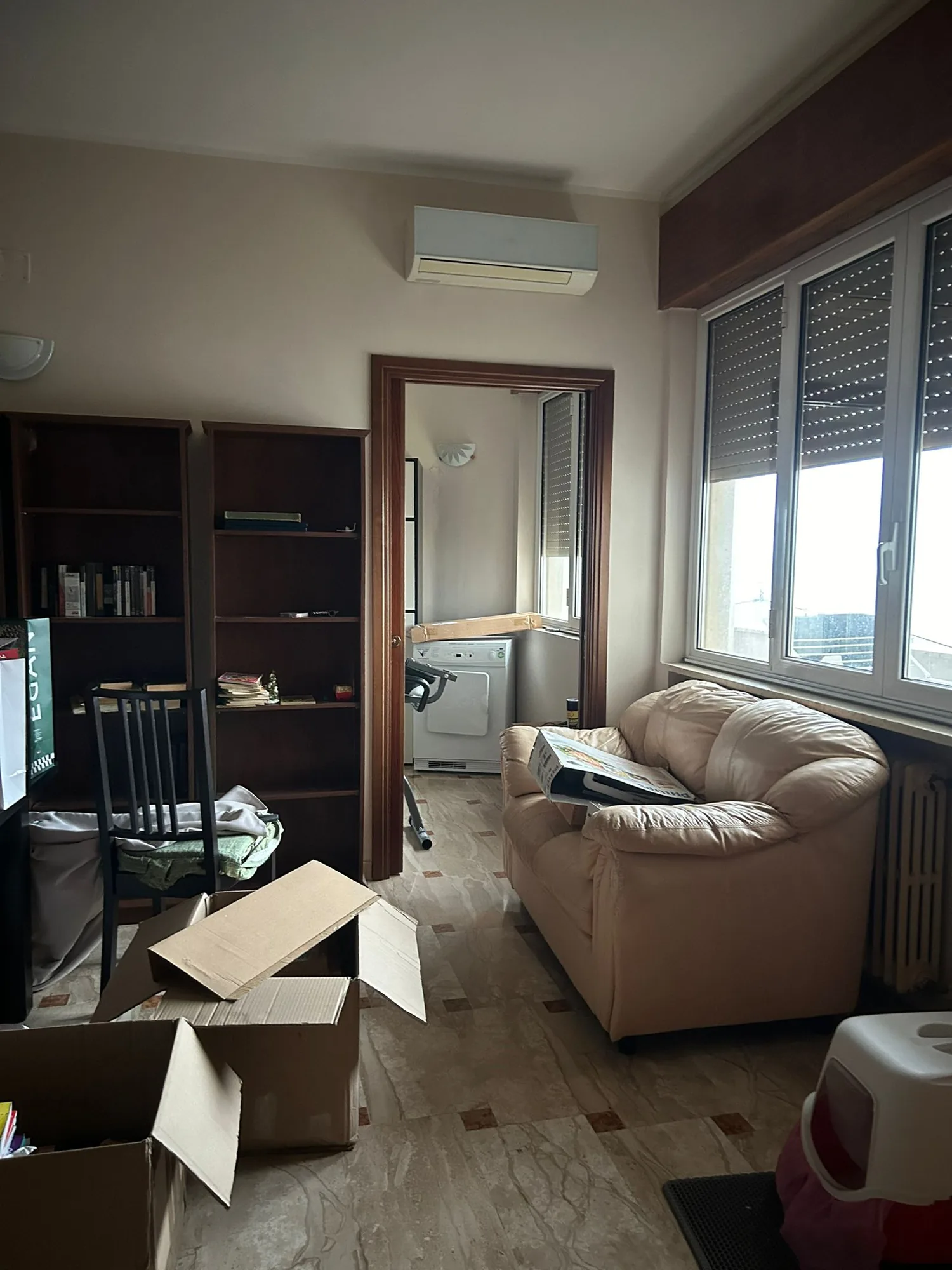 Living room before the intervention, with dark wood bookcase and furnishings to be replaced