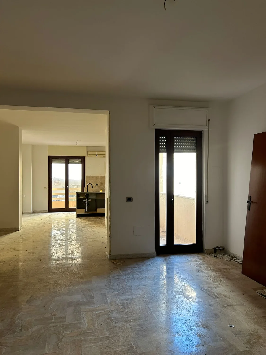 Stanza vuota prima dei lavori, con pavimento originale e apertura verso la cucina