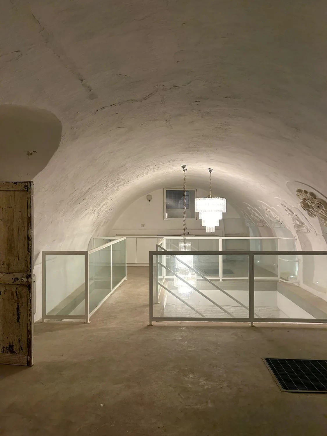 Vista dal soppalco, con balaustra in vetro, lampade a sospensione e cucina a vista