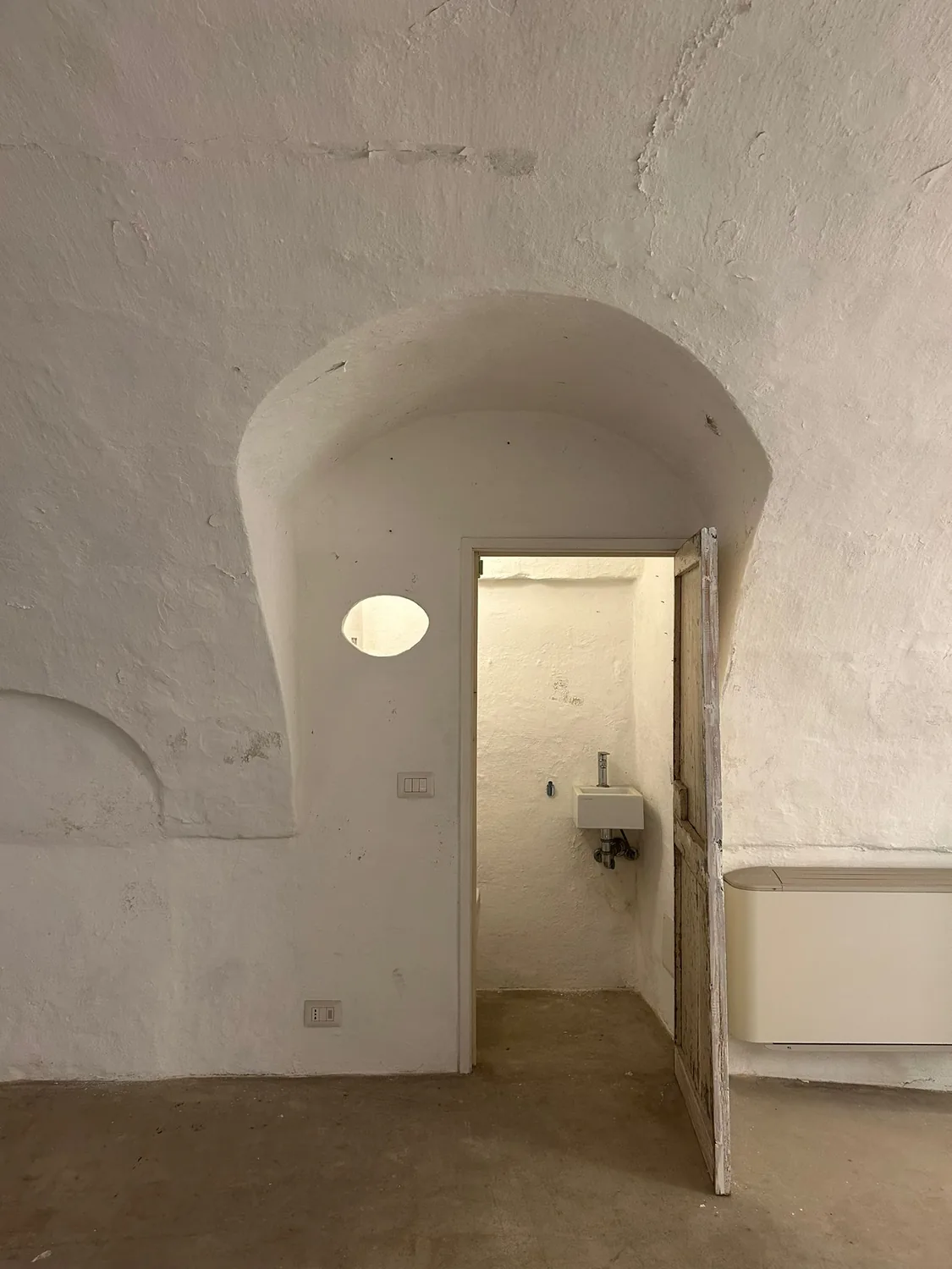 Apertura ad arco nella parete imbiancata, con porta verso un piccolo bagno