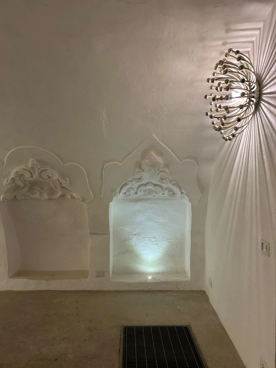 Le nicchie decorate a stucchi sulle pareti imbiancate, con lampada a parete di design
