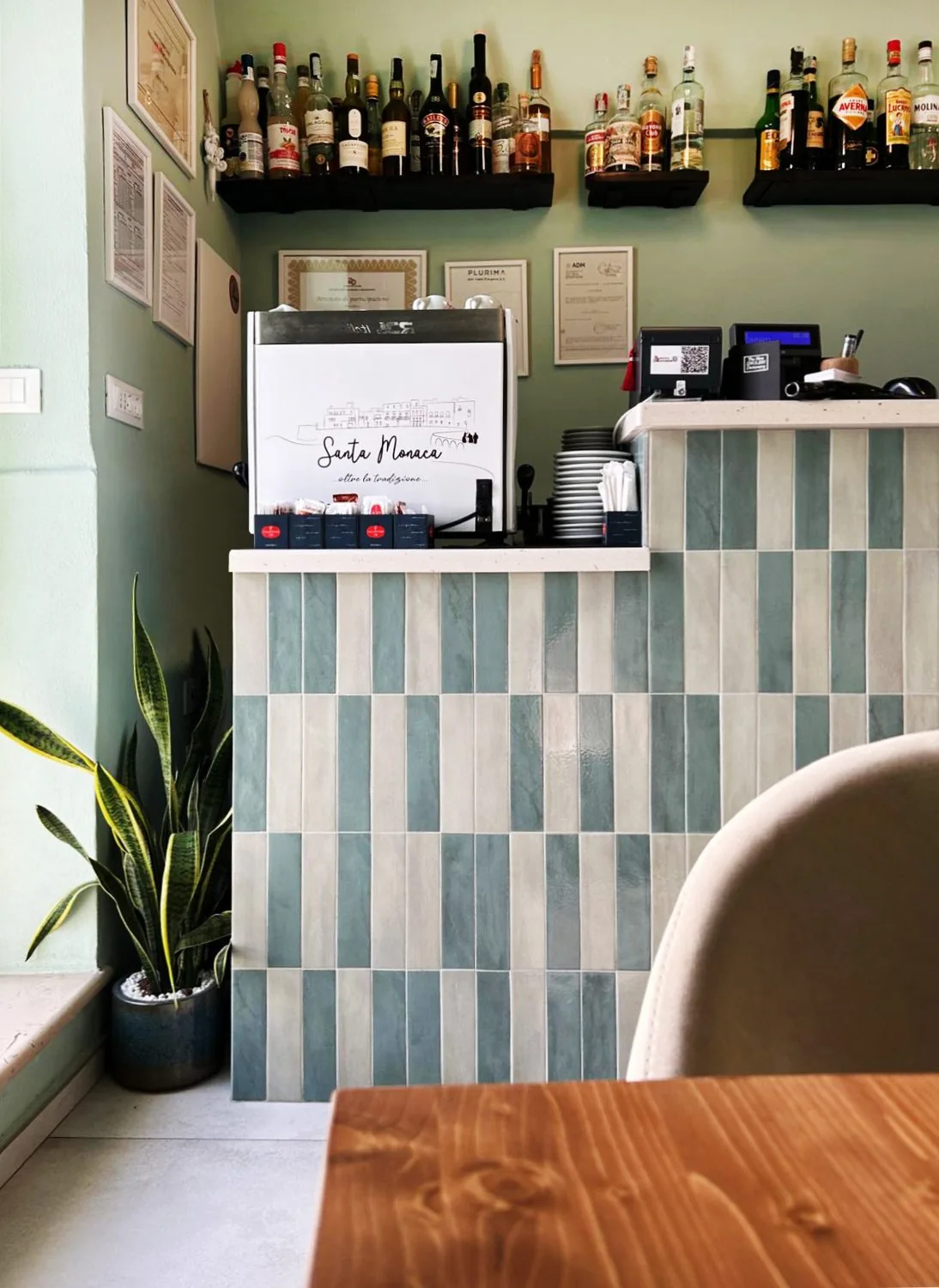 Il bancone del bar, con rivestimento a piastrelle bicolore e mensole con bottiglie
