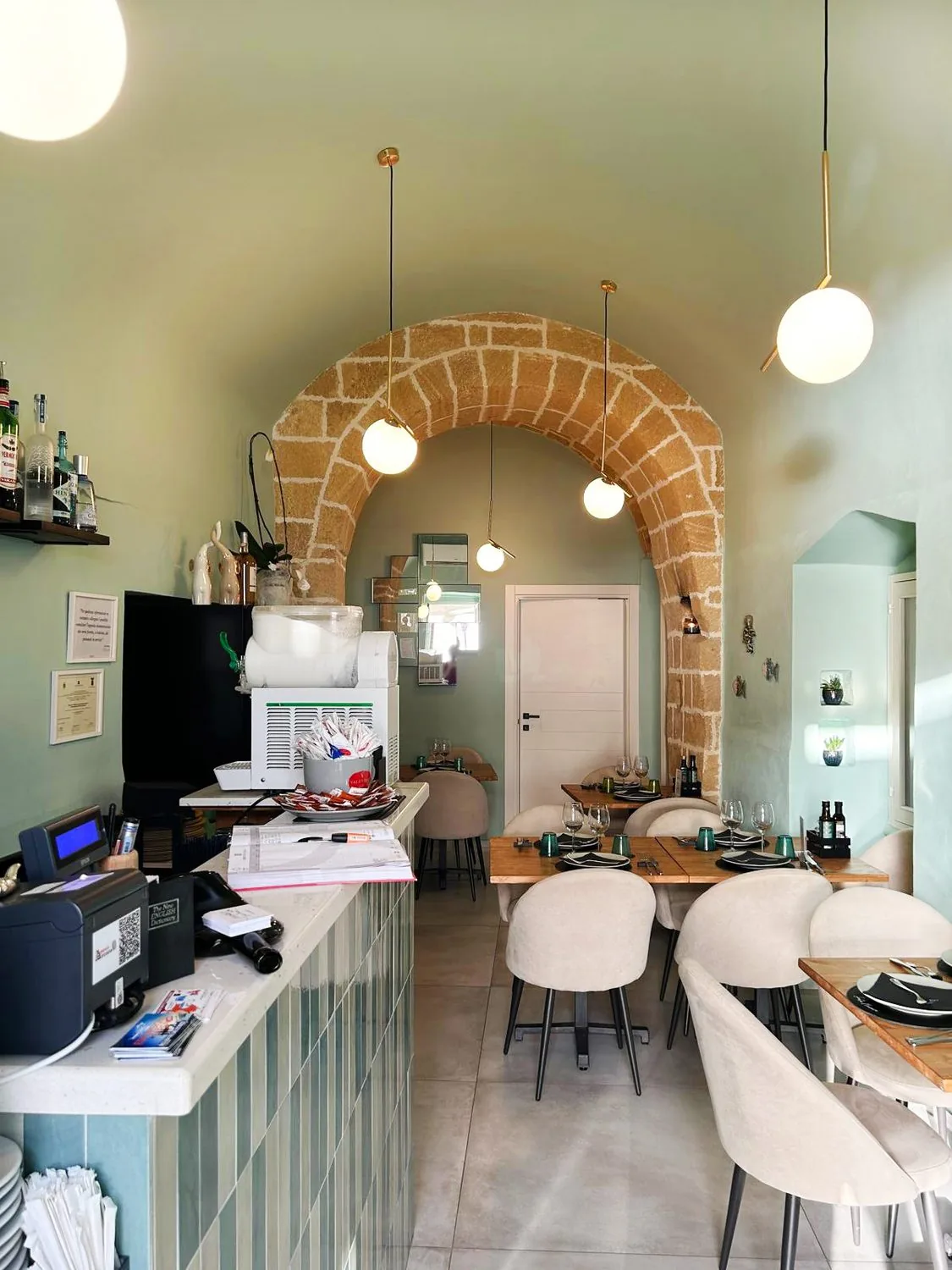 La sala interna, con tavoli apparecchiati, bancone, lampade a sospensione e arco in pietra