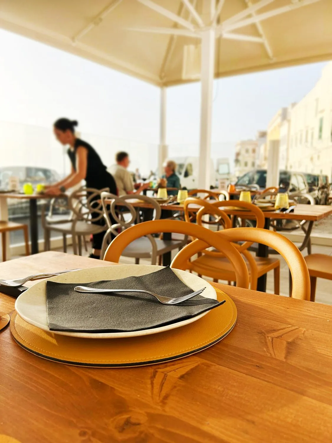 Lo spazio esterno coperto, con tavoli in legno e sedie chiare sotto un grande ombrellone